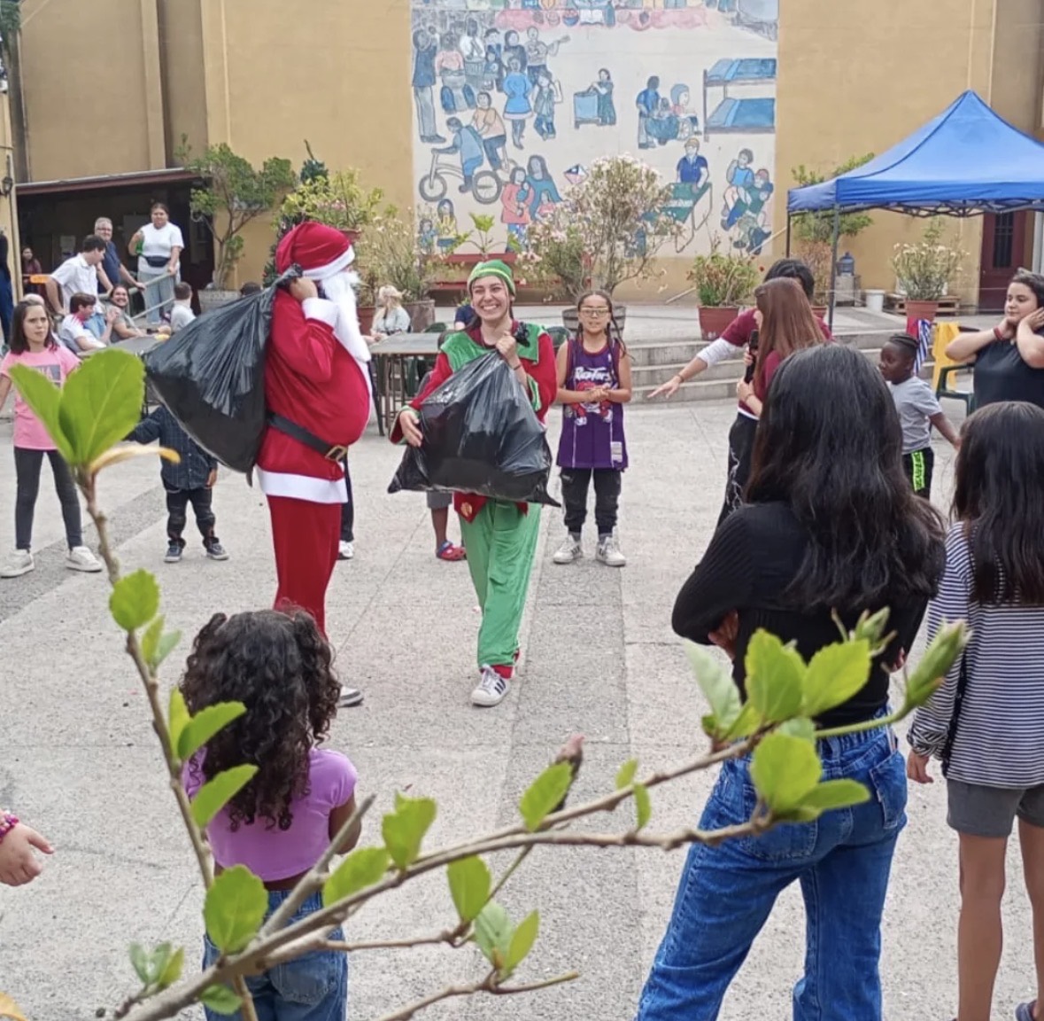 Viejito pascuero y un ayudante llegando con los sacos de juguetes, rodeados de niños y niñas de la población